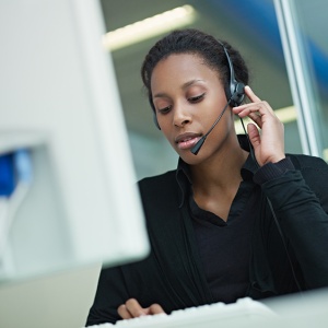 female african american customer service representative with headset typing on computer. Horizontal shape, front view, waist up